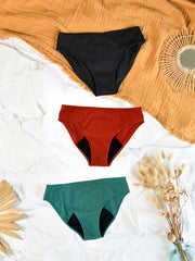 lot de 3 culottes de règles colorés , rouge, verte, noire à plat sur un lit. 